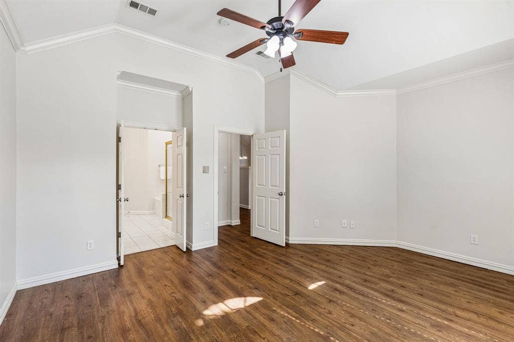 6852 High Field Trail, Plano, TX 75023 Spacious bedroom featuring rich wood-finish flooring, ceiling fan with integrated lighting, white crown molding, and multiple closet entries