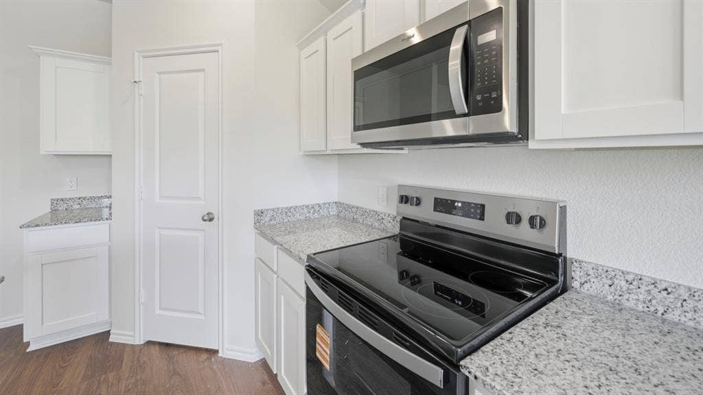 5032 Shumard Drive, Lindale, TX 75771 Kitchen featuring a stainless steel microwave, black electric range, white cabinetry, light-toned countertops, and wood-finish flooring