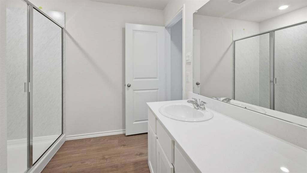 5032 Shumard Drive, Lindale, TX 75771 Bathroom featuring a single vanity with a white countertop and oval undermount sink, chrome faucet, wood-finish flooring, and a glass-enclosed shower