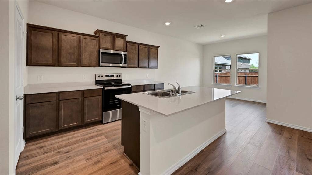 5024 Shumard Drive, Lindale, TX 75706 Kitchen featuring an expansive island with an undermount double-basin sink, dark wood-finish cabinetry, stainless steel appliances, and wood-finish flooring