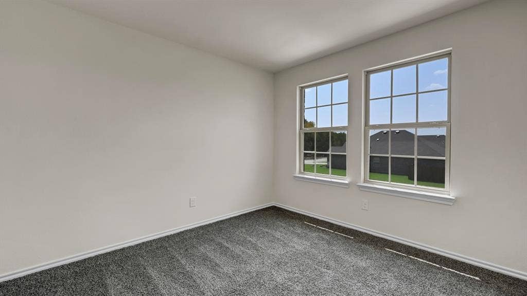 5024 Shumard Drive, Lindale, TX 75706 Interior room featuring two vertical windows with grid inserts and white trim, neutral white walls, and gray textured carpeting
