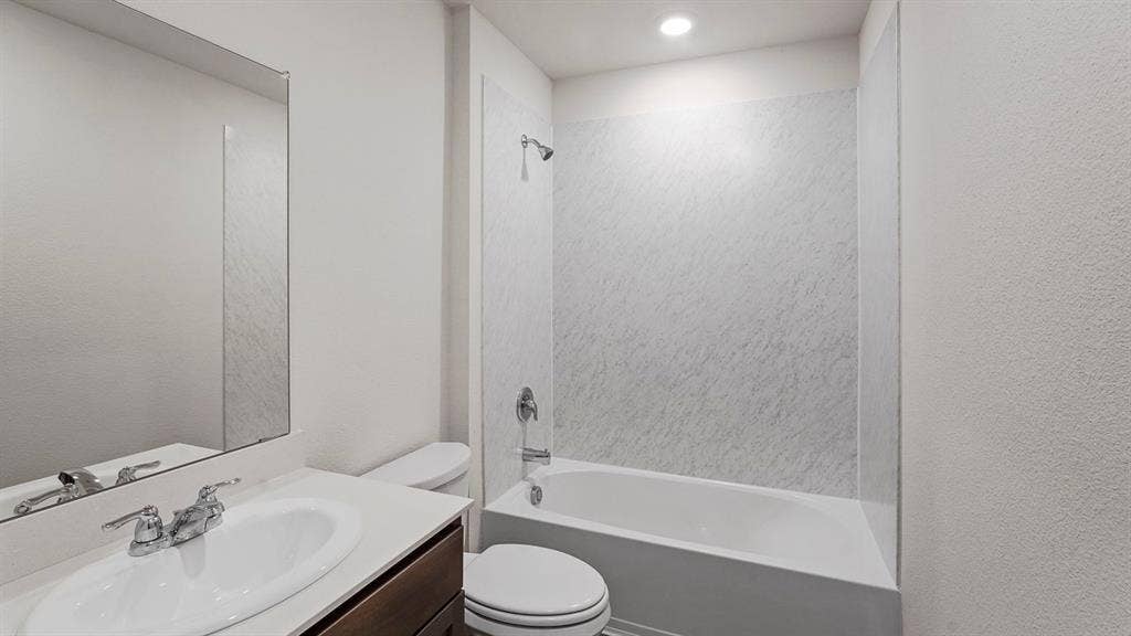Bathroom featuring a white bathtub with a textured shower surround, a chrome shower fixture, and a built-in vanity with a white countertop and undermount sink