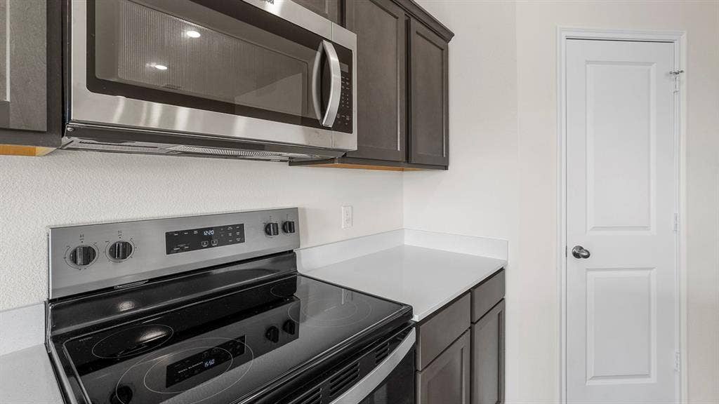 Modern kitchen featuring a stainless steel microwave, electric range with a ceramic cooktop, dark wood-finish cabinetry, and light-toned countertops