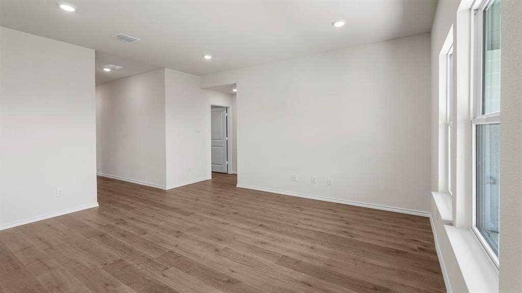 Spacious interior room featuring wood-finish flooring, recessed lighting, and multiple windows with white trim