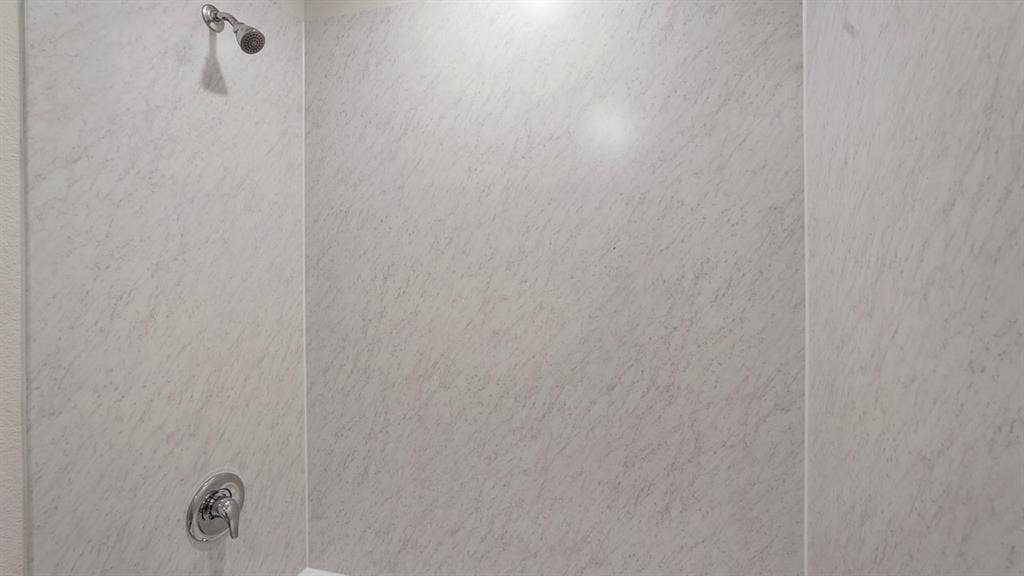 Shower stall featuring light-toned, textured wall panels and chrome fixtures
