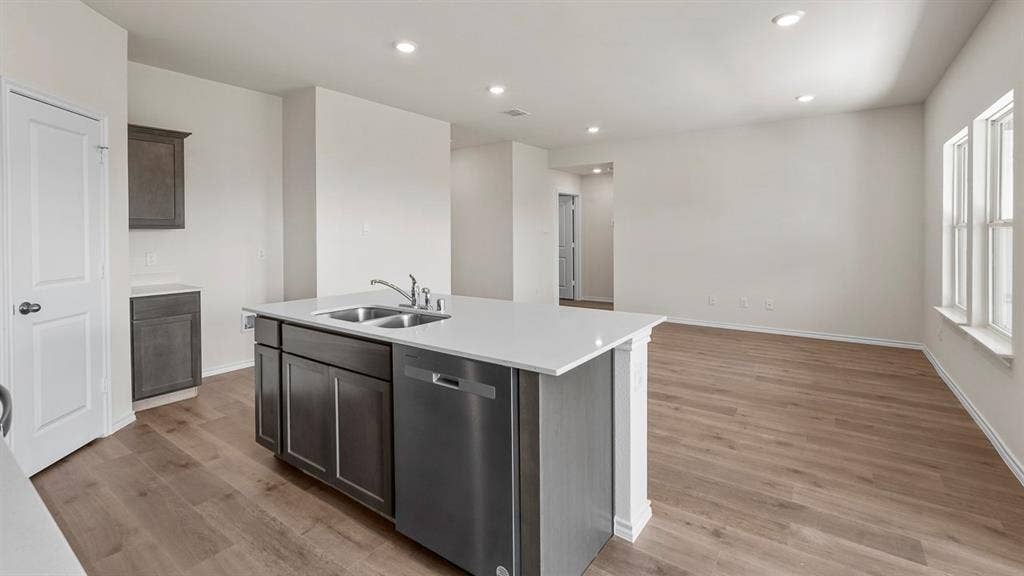 Open-concept kitchen featuring a center island with a double basin sink and stainless steel dishwasher, white countertops, wood-finish flooring, and recessed lighting