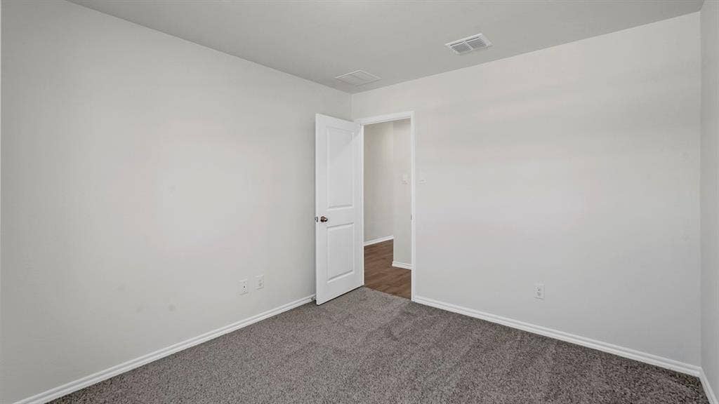 Carpeted room featuring white walls, white trim, a white interior door with a silver knob, and a ceiling vent