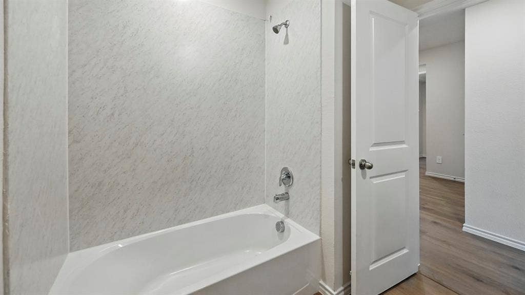 5008 Shumard Drive, Lindale, TX 75771 White bathtub with a chrome showerhead and faucet, surrounded by textured white wall panels