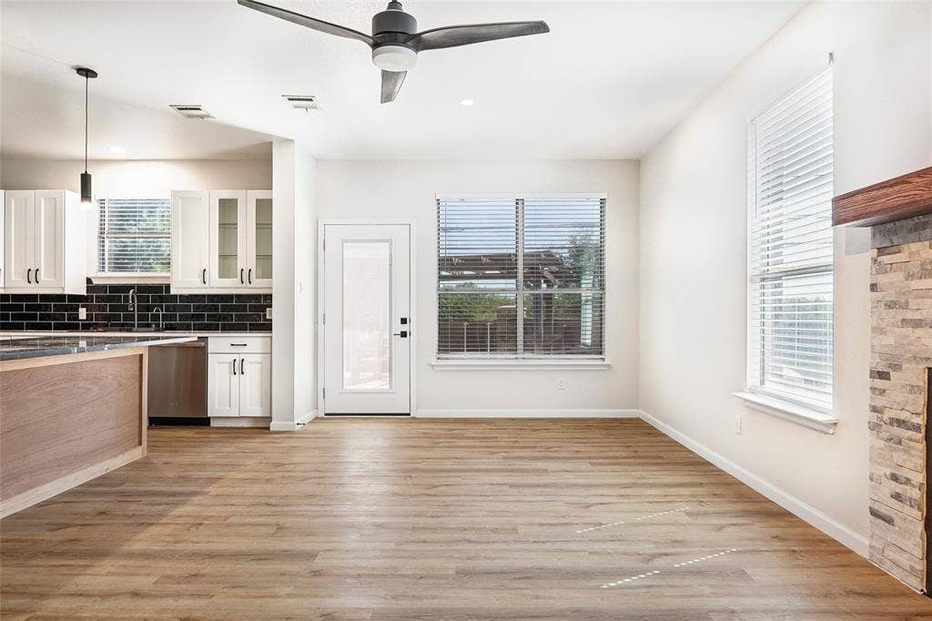Wood-finish flooring throughout, bright white walls, modern ceiling fan, and stone-clad fireplace with a wood mantle