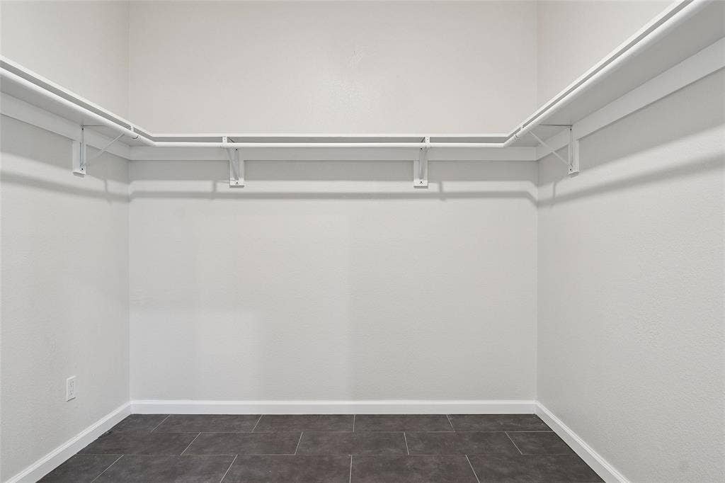 Walk-in closet with white walls, dark tile flooring, and a built-in white shelving system