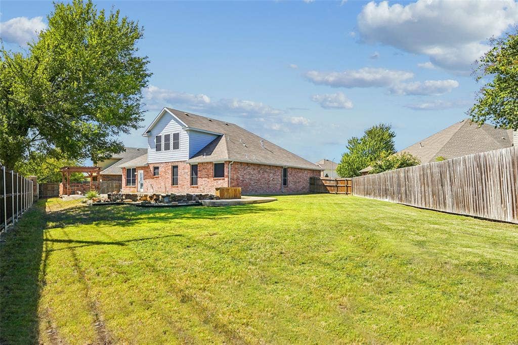Expansive backyard featuring a large grass area, brick exterior, and wood fencing