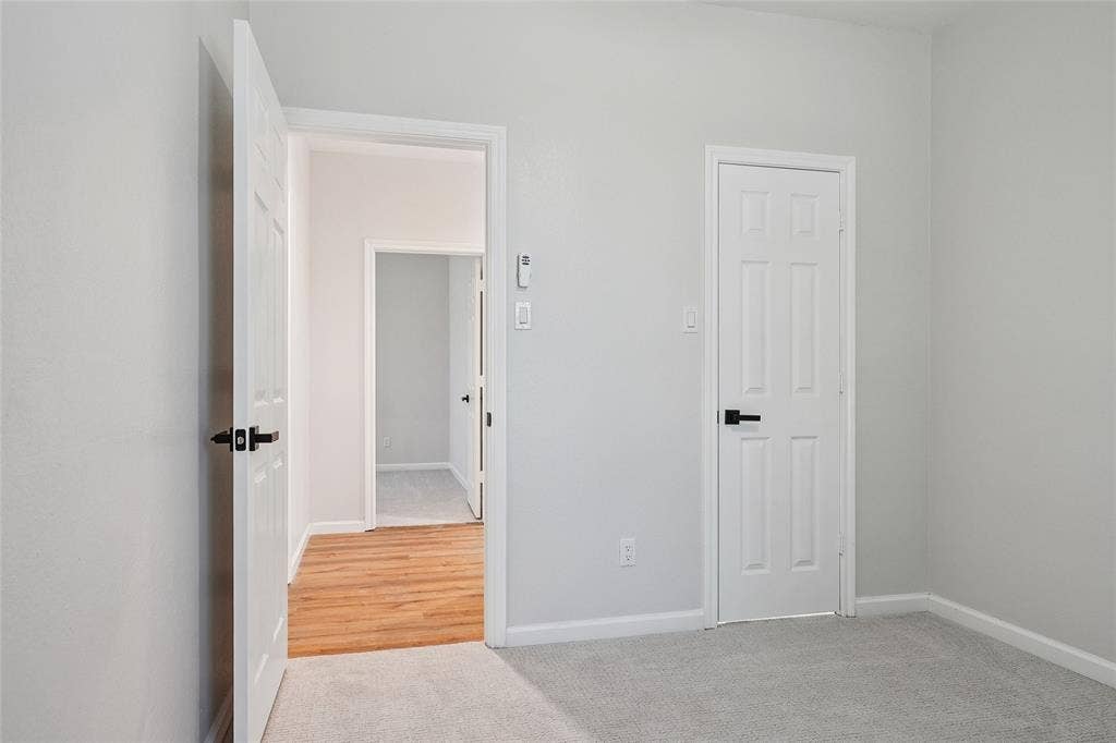 Light gray wall paint, paneled interior doors, matte black door hardware, light gray carpet, and wood-finish flooring
