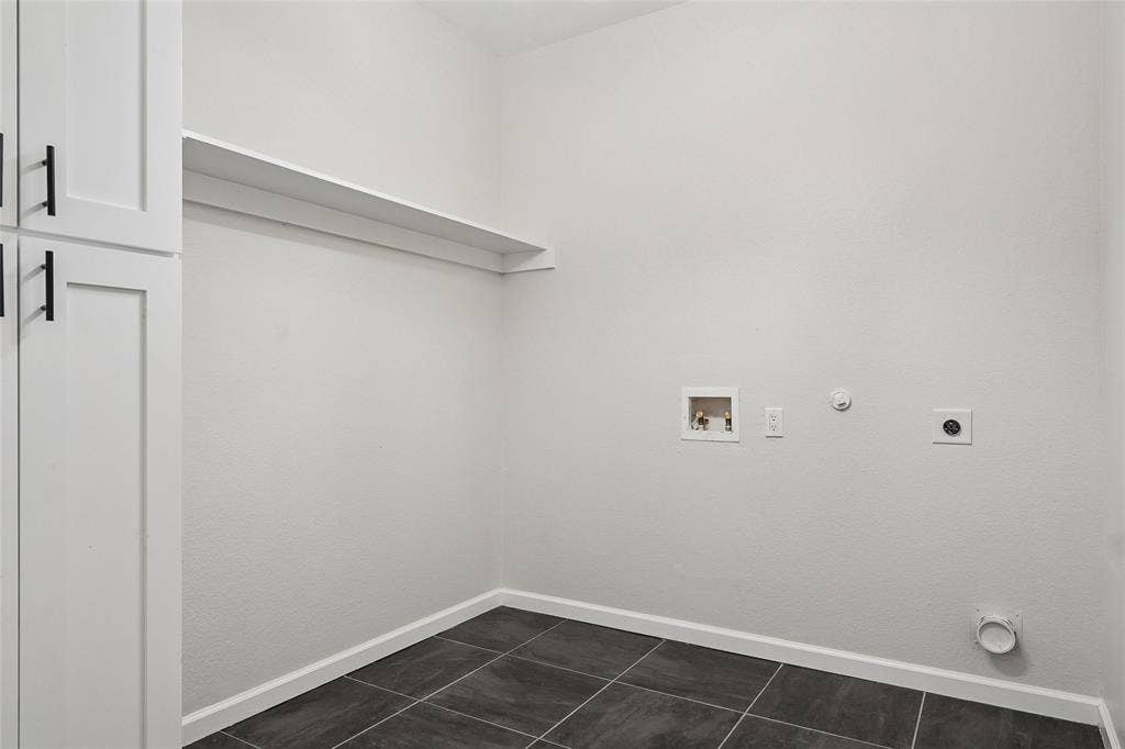 Built-in cabinetry with matte black hardware, white wall shelving, and dark tile flooring