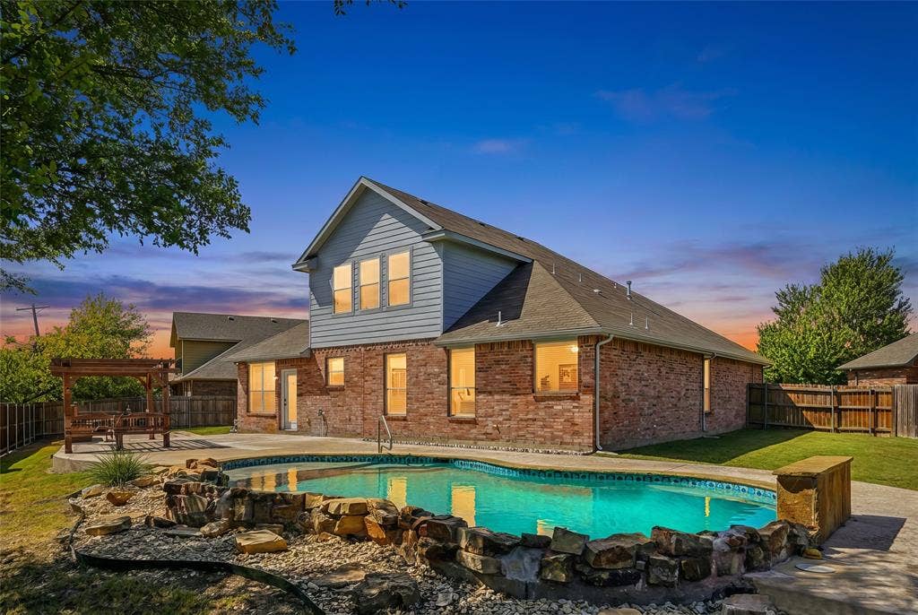 Brick and siding exterior with a pool, integrated rock water feature, and a wooden pergola structure