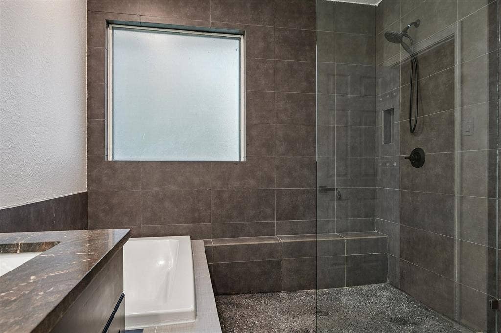 Walk-in shower with dark tile surround, built-in bench, and clear glass enclosure