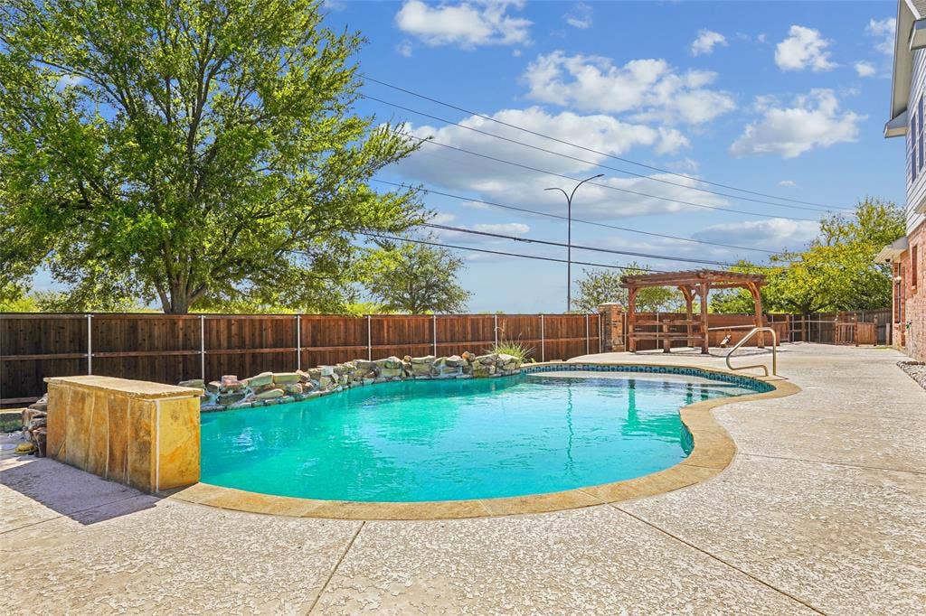 Freeform swimming pool with rock waterfall feature, concrete decking, and wood privacy fencing