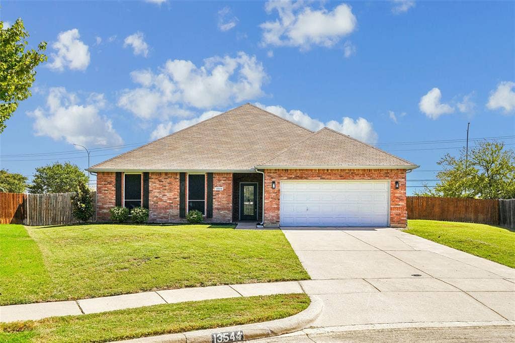 Brick exterior with dark shutters, attached two-car garage, concrete driveway, and front lawn