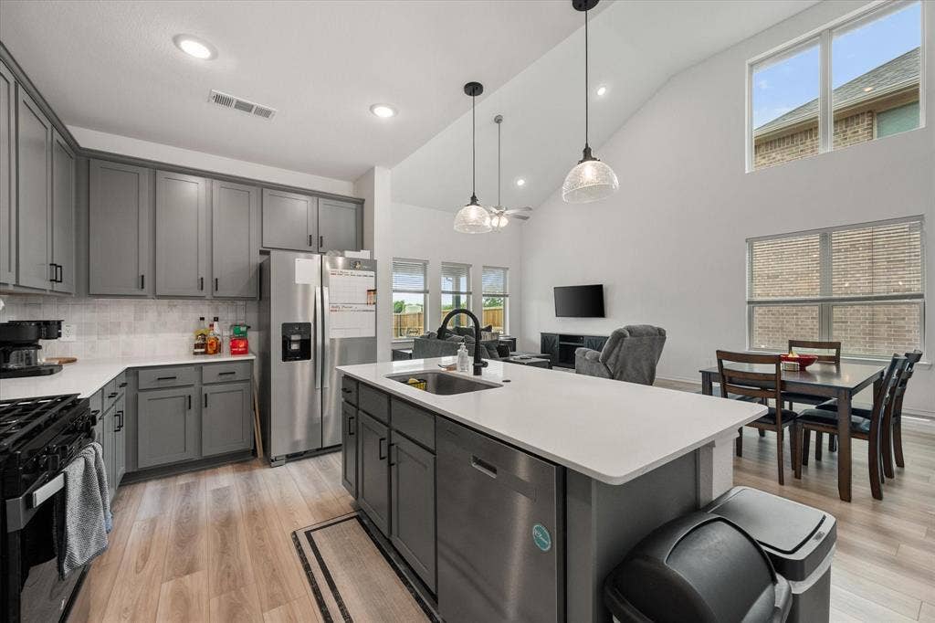 2325 Volans Drive, Haslet, TX 76052 Open-concept kitchen featuring gray cabinetry, stainless steel appliances, a center island with sink, quartz countertops, and wood-finish flooring