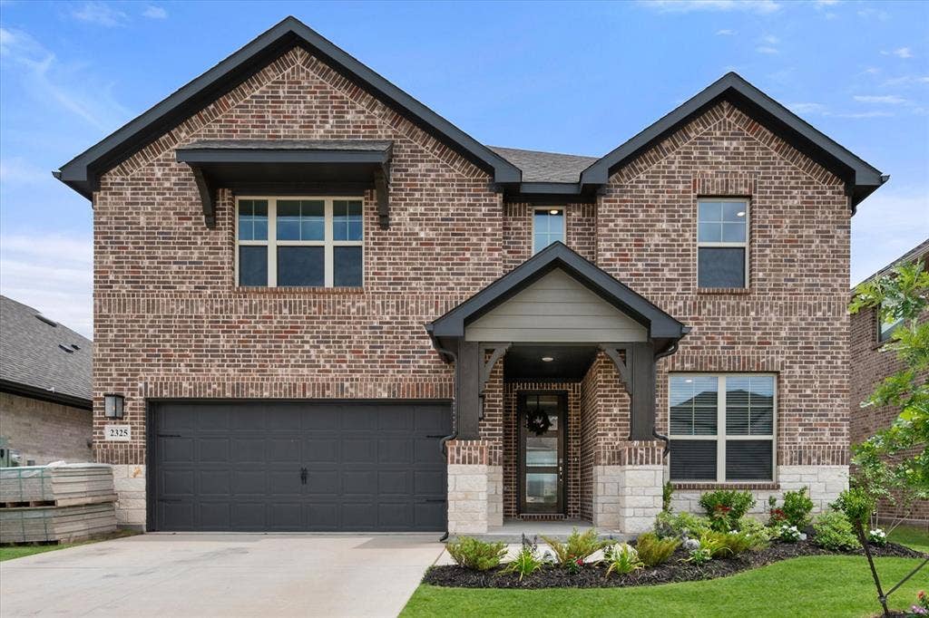2325 Volans Drive, Haslet, TX 76052 Brick and stone exterior featuring a covered entry porch with decorative columns, an attached two-car garage, and a manicured front lawn with established landscaping