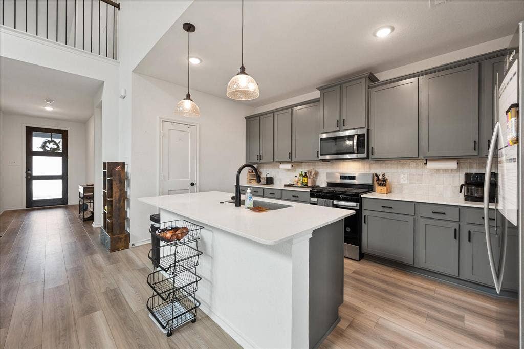 2325 Volans Drive, Haslet, TX 76052 Modern kitchen featuring gray cabinetry, stainless steel appliances, a center island with a white countertop, and wood-finish flooring