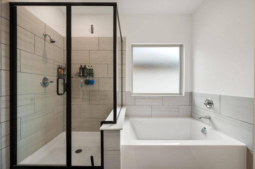 2325 Volans Drive, Haslet, TX 76052 Modern bathroom featuring a walk-in shower with black-framed glass enclosure, white tile surround, and a built-in bathtub with a frosted window