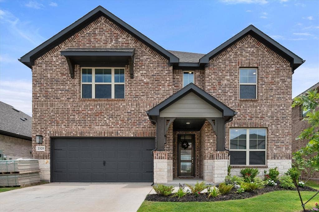 2325 Volans Drive, Haslet, TX 76052 Two-story brick facade featuring a dark gray garage door, covered entry with stone accents, dark trim, and an awning window feature
