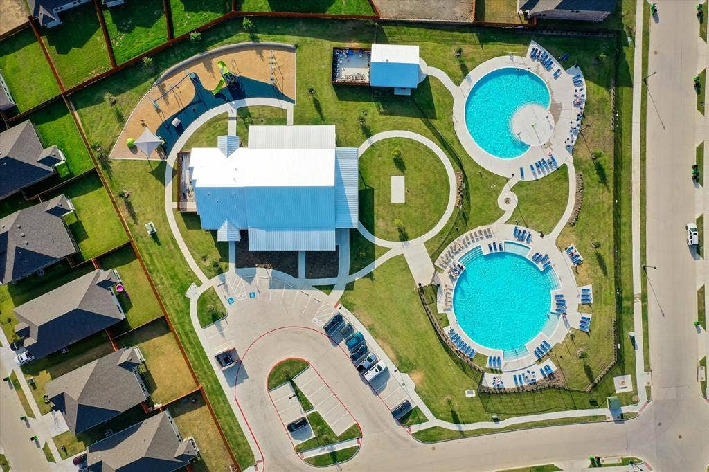 2325 Volans Drive, Haslet, TX 76052 Community recreation area featuring a central building, two swimming pools with surrounding lounge chairs, a playground with shaded structures, and open green spaces