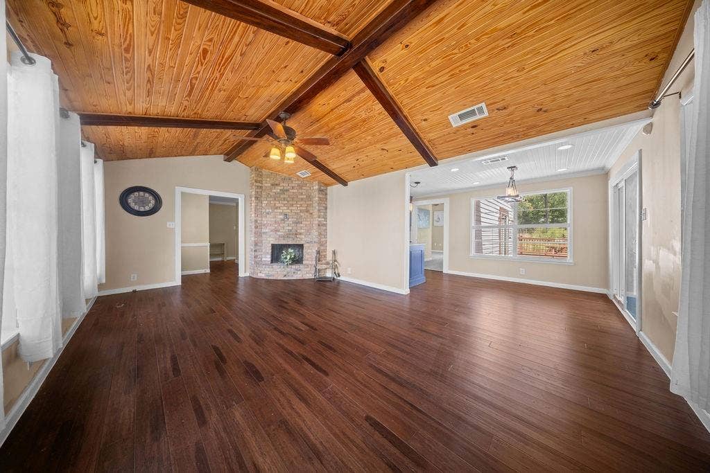 Spacious interior featuring wood-finish flooring, a brick-surround fireplace, and a wood plank vaulted ceiling with exposed beams