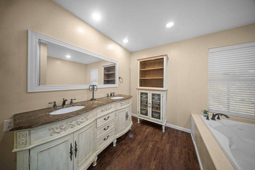 Bathroom featuring a dual vanity with a decorative antique white finish, a stone countertop, and two undermount sinks