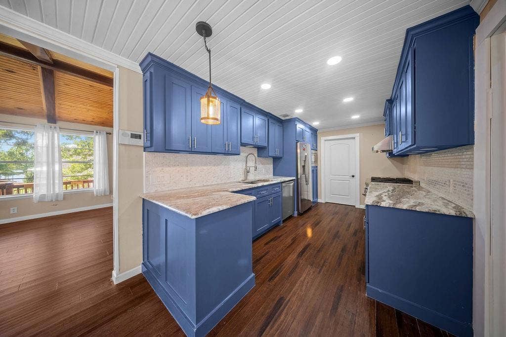 Kitchen featuring blue cabinetry, stone countertops, stainless steel appliances, a tile backsplash, and wood-finish flooring
