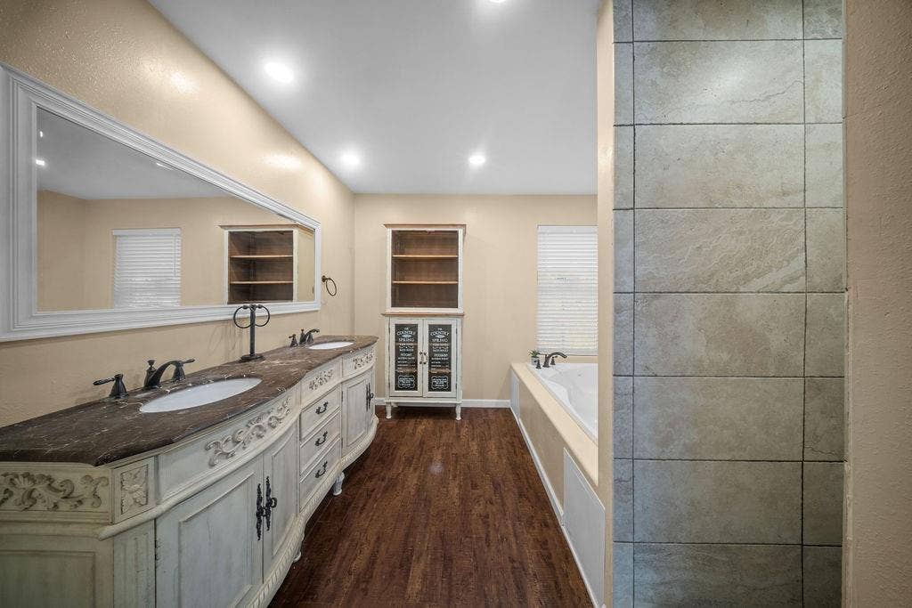 Spacious bathroom featuring a dual vanity with a curved, ornate base, dark countertops, and undermount sinks
