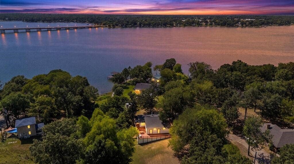 Waterfront property with a private dock, lush tree canopy, and a large deck