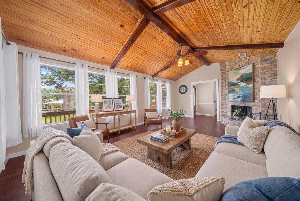 Vaulted wood-plank ceiling with exposed beams, full-height brick fireplace, rich wood-finish flooring, and multiple large windows