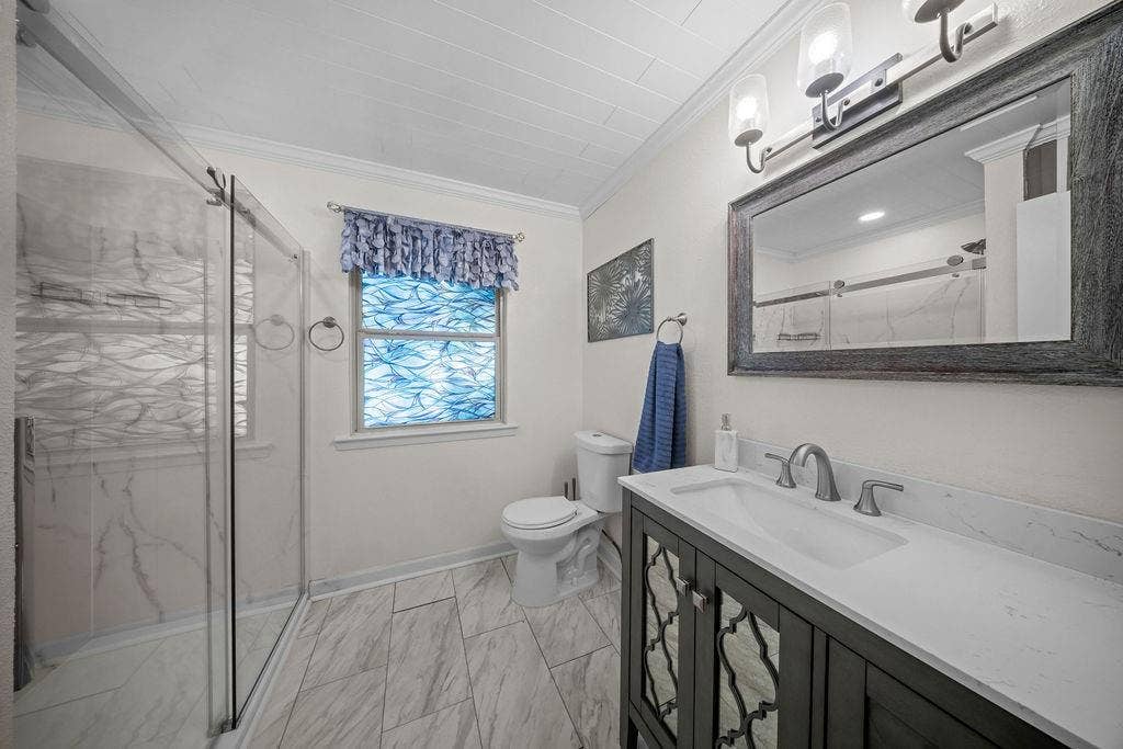 Contemporary bathroom featuring a glass-enclosed shower with marble-look tile surround, a single vanity with a quartz countertop, and a decorative framed mirror