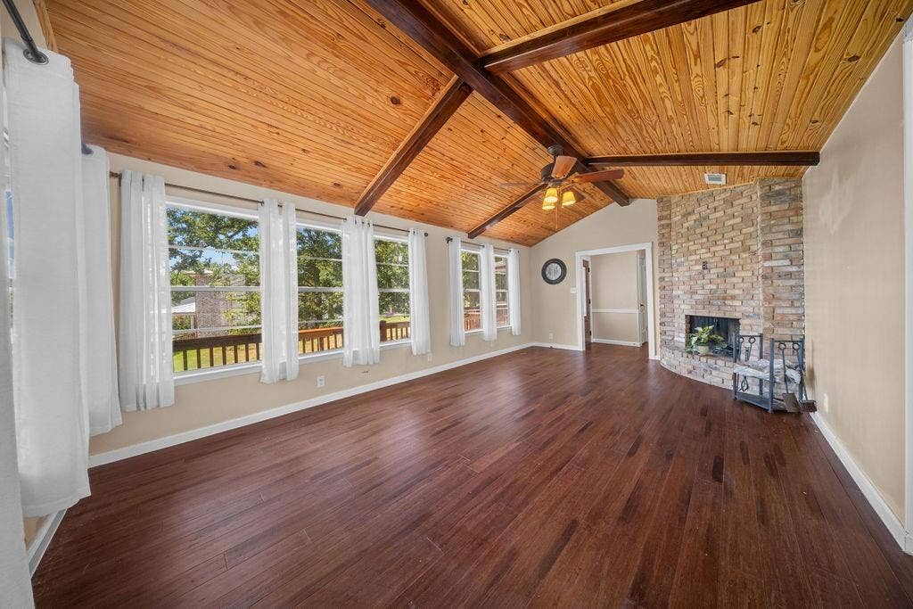 Spacious living area featuring a vaulted wood-paneled ceiling with exposed beams, wood-finish flooring, and a stone-clad fireplace