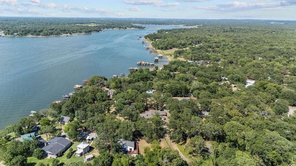 Expansive waterfront property featuring a substantial body of water, lush green tree cover, multiple docks, and varied residential structures