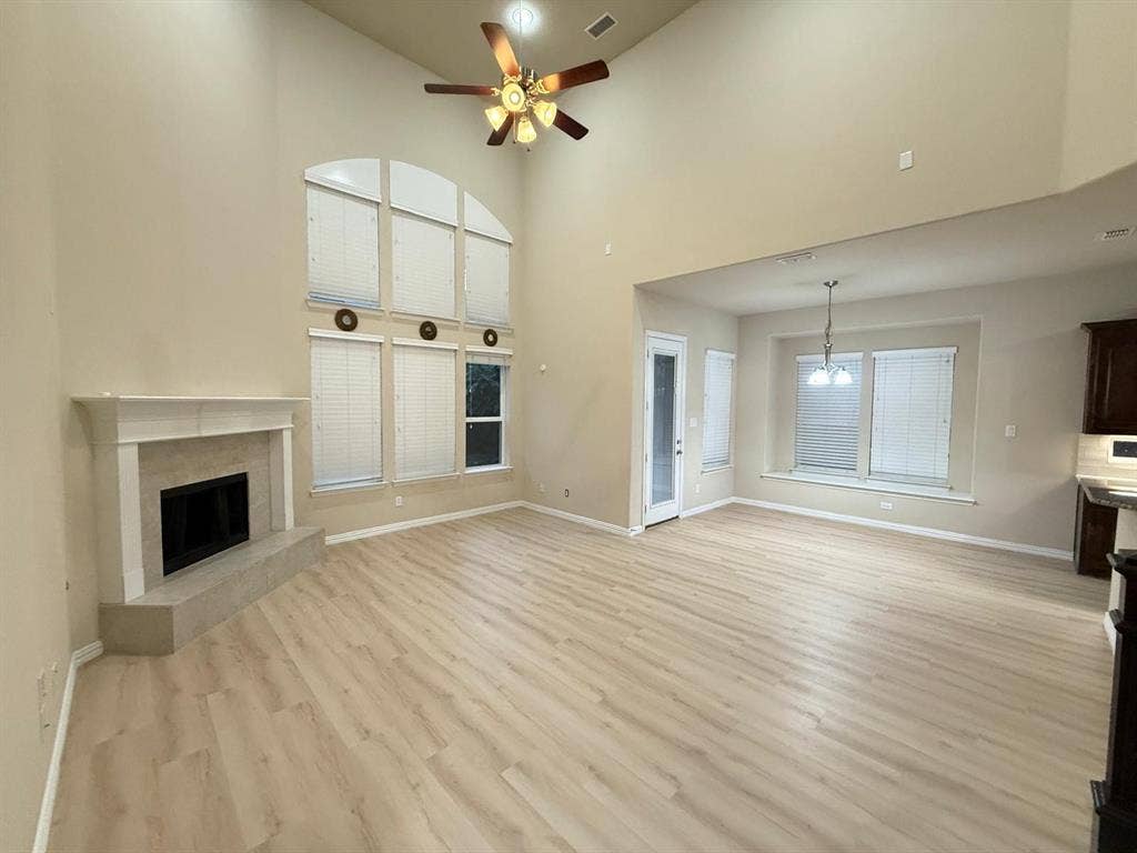 Open-concept living area featuring high vaulted ceilings, light wood-finish flooring, a contemporary fireplace with a mantle, and large arched windows with blinds