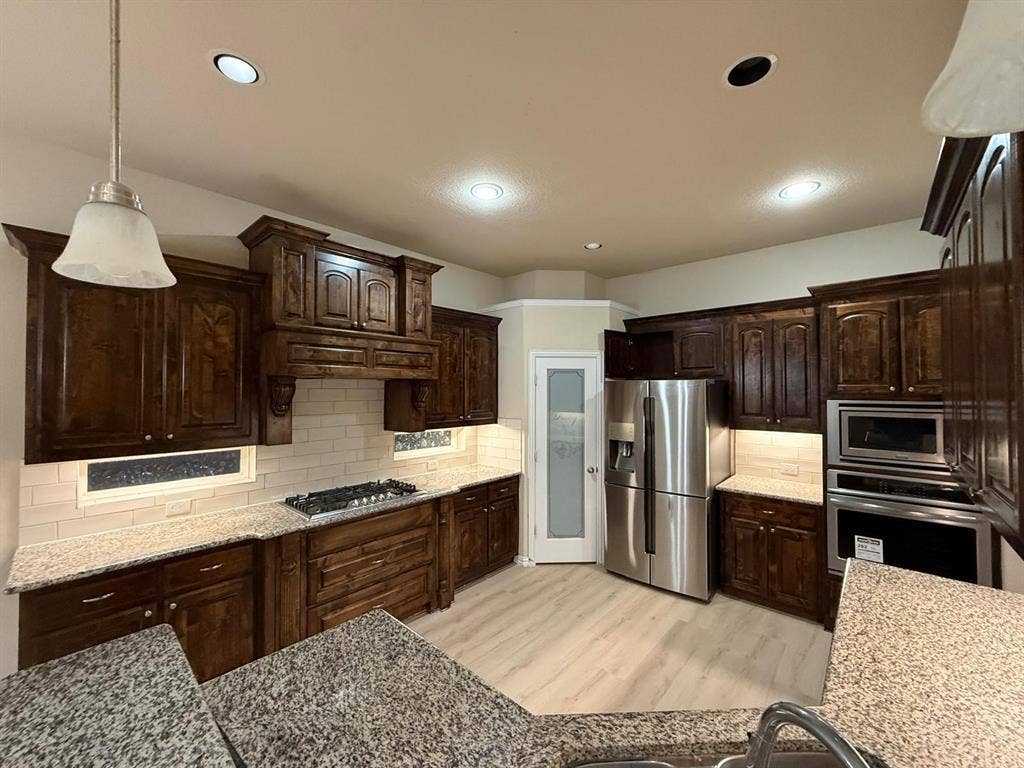 Kitchen featuring rich wood cabinetry, granite countertops, a tiled backsplash, and stainless steel appliances