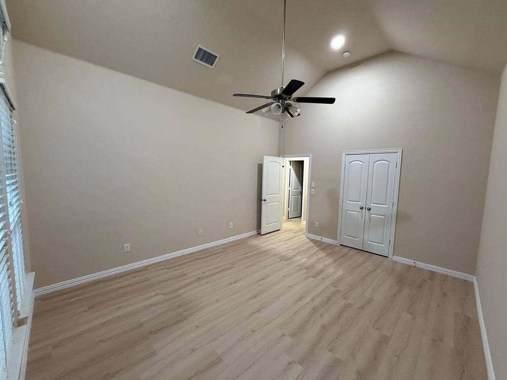 Spacious room featuring vaulted ceilings, light wood-finish flooring, a ceiling fan with integrated lighting, and multiple white paneled doors
