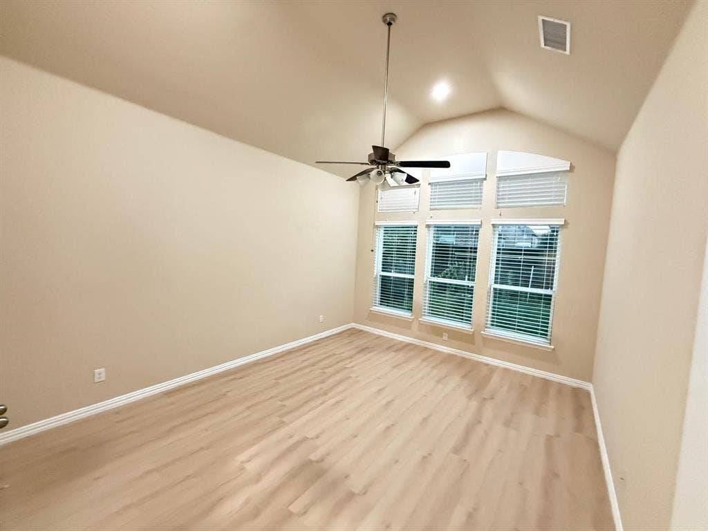 Spacious room featuring vaulted ceilings, an abundance of natural light from multiple windows, light wood-finish flooring, and a ceiling fan with integrated lighting