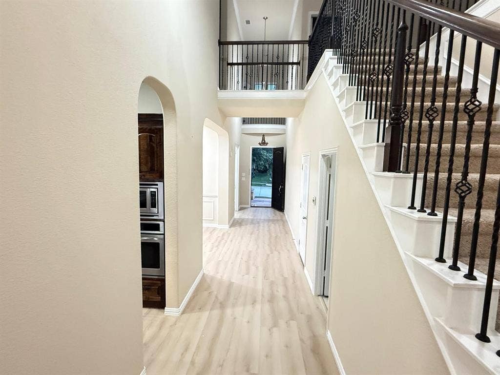 Grand foyer featuring a carpeted staircase with ornate wrought iron balusters and wood handrails, flanked by light wood-finish flooring