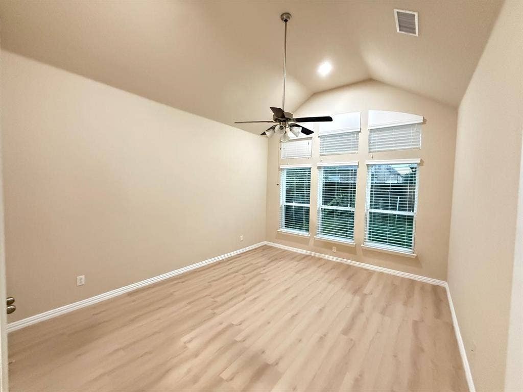 Vaulted ceiling room featuring light wood-finish flooring, a ceiling fan with light fixture, and a wall of three large windows