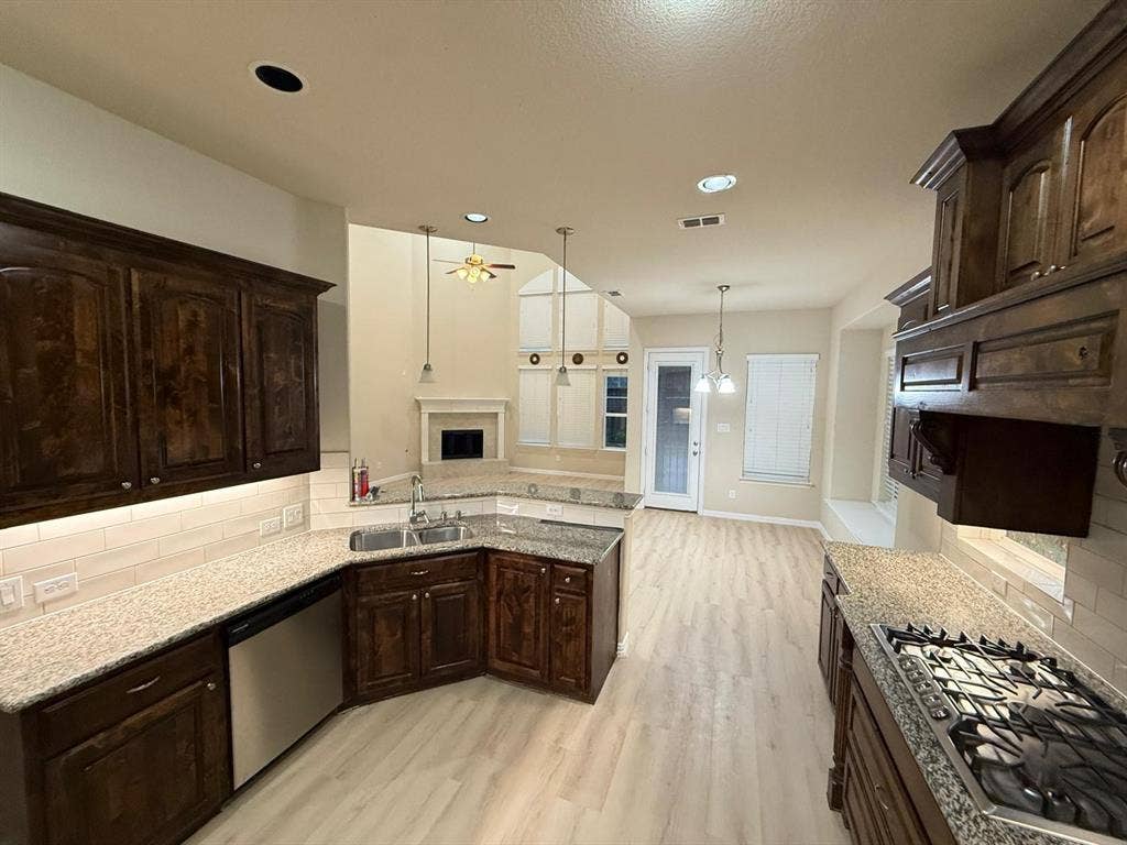 Kitchen featuring dark wood cabinetry, granite-finish countertops, stainless steel appliances, and light wood-finish flooring