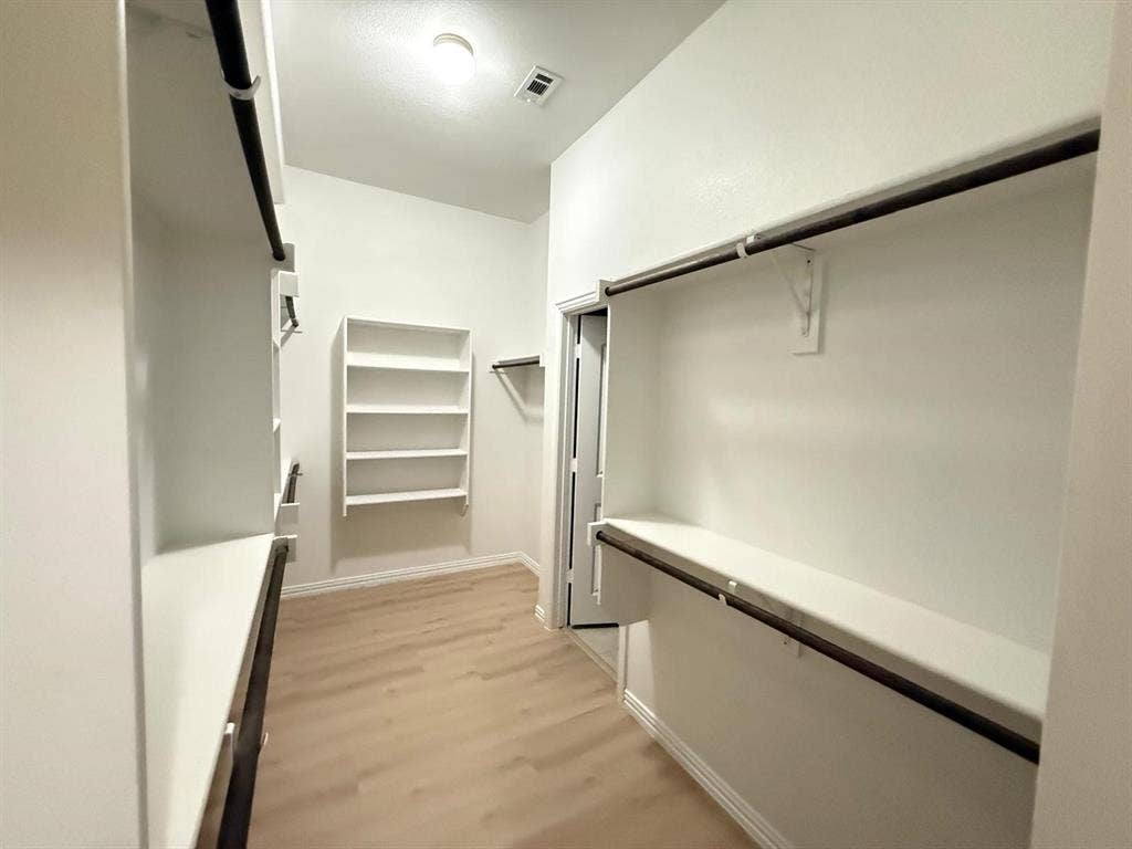 Expansive closet featuring wood-finish flooring, white built-in shelving, and multiple hanging rods