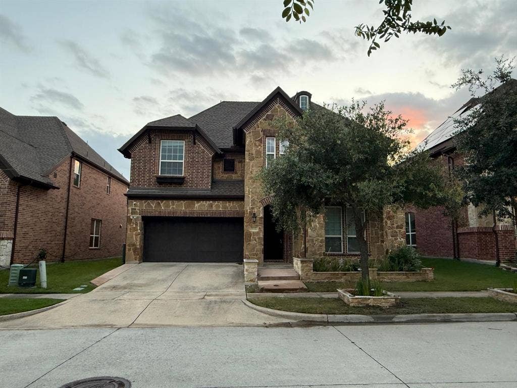 Stone and brick façade residence featuring a two-car garage, mature front yard landscaping, and a concrete driveway