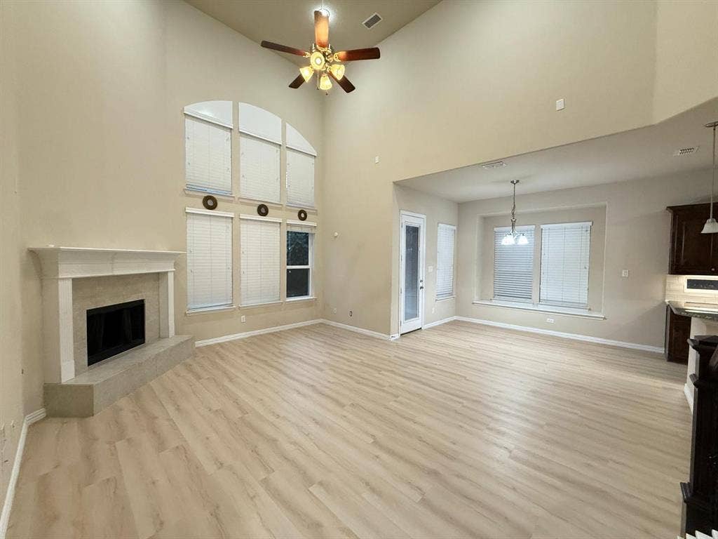 Spacious living area featuring high vaulted ceilings, light wood-finish flooring, and a fireplace with a stone surround