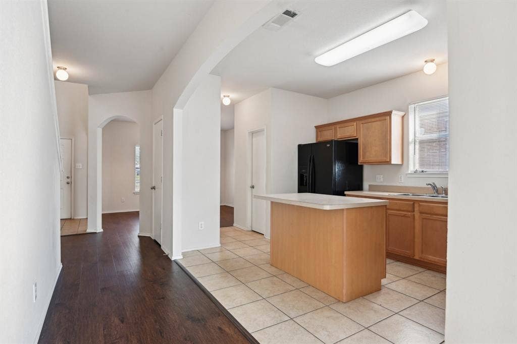 3019 Appaloosa Drive, Dallas, TX 75237 Kitchen featuring black fridge, a healthy amount of sunlight, a kitchen island, and light tile patterned floors