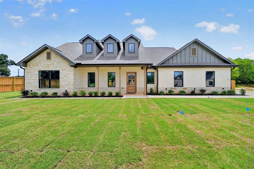 301 Grace Lane, Athens, TX 75751 Stone and brick exterior with dark-framed windows, a prominent wood-finish entry door, multiple dormer windows, and a landscaped foundation planting
