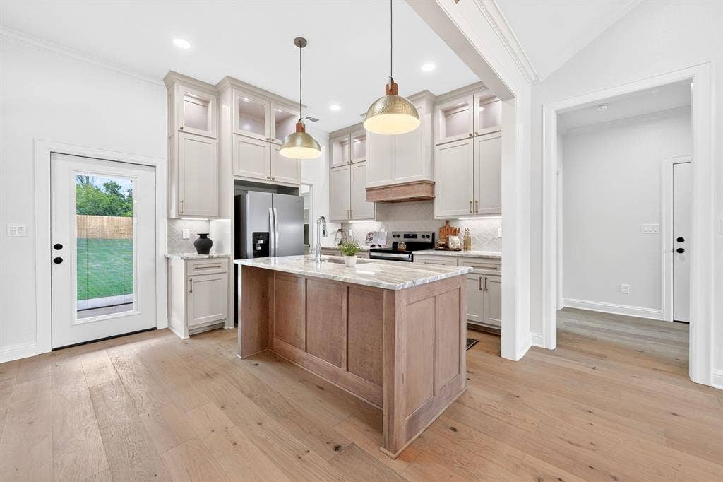301 Grace Lane, Athens, TX 75751 Kitchen featuring a central island with a stone countertop, light wood-finish flooring, custom cabinetry with under-cabinet lighting, stainless steel appliances, and a full-light door to the exterior