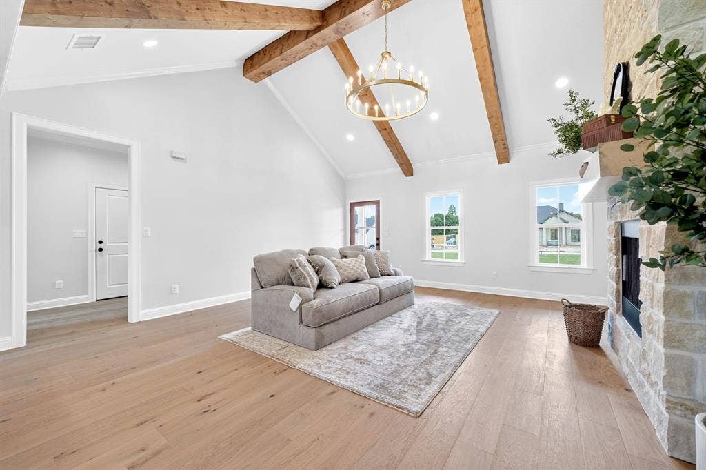 301 Grace Lane, Athens, TX 75751 Vaulted ceiling with exposed wood beams, light wood-finish flooring, stone fireplace with dark firebox, recessed lighting, and a prominent chandelier